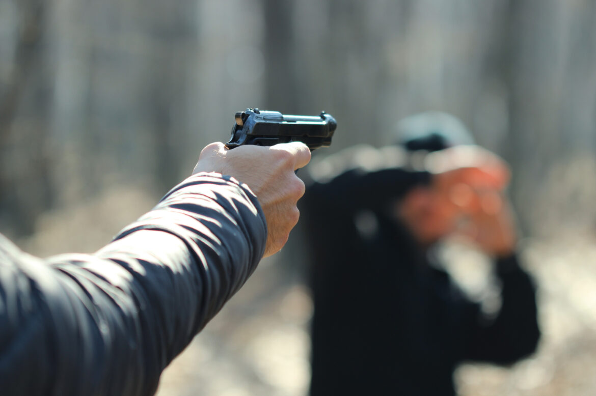 Cropped Hand Of Man Aiming With Gun At Person